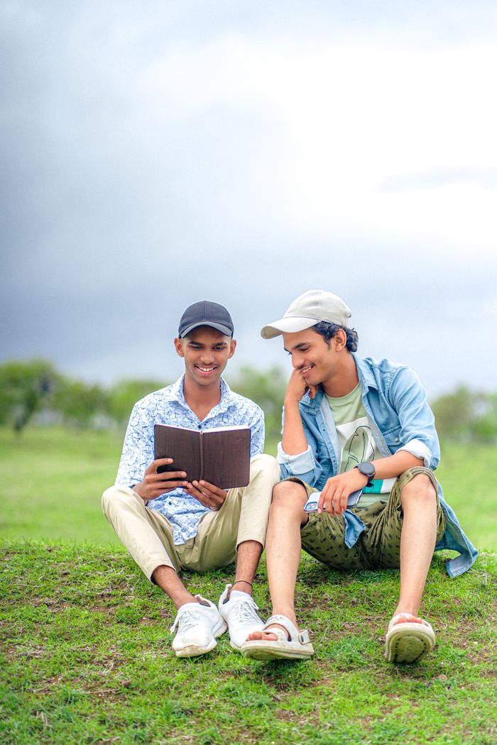 Mastering the First Impression: Your intriguing post title goes here Two young men casually reading a book together outdoors, enjoying a relaxed moment on a sunny day.
